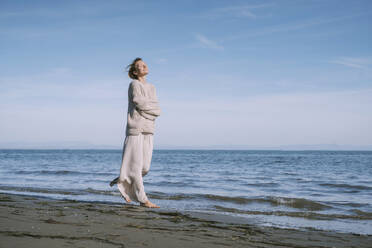 Solitude woman with arms crossed walking on shore at beach - NDEF00506