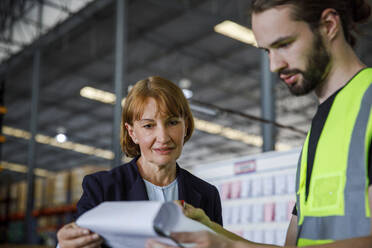 Manager and colleague examining checklist at warehouse - IKF00053