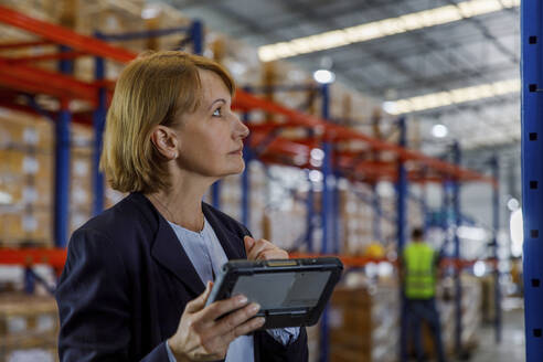 Thoughtful manager standing with tablet PC in warehouse - IKF00074