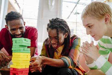 Lächelnde junge Freunde, die zu Hause ein Spiel zum Entfernen von Blöcken spielen - MDOF01005