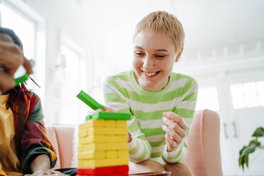 Glückliche junge blonde Frau spielt mit Freunden zu Hause ein Spiel mit Blöcken - MDOF01021