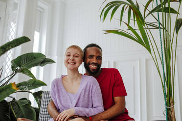 Glückliches Paar sitzt vor einer weißen Wand zu Hause - MDOF01027