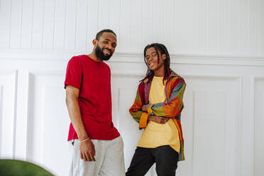 Smiling young friends standing in front of wall at home - MDOF01029