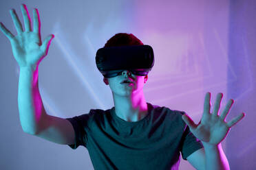 Junger Mann mit Virtual-Reality-Simulator gestikuliert vor einer Wand - ABIF01913