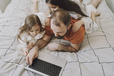 Töchter mit Vater bei der Benutzung eines Laptops auf dem Bett zu Hause - VBUF00283