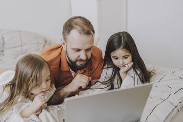 Vater und Töchter schauen auf einen Laptop auf dem Bett - VBUF00284