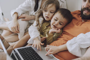 Glückliche Familie, die zu Hause gemeinsam einen Laptop benutzt - VBUF00286