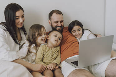 Lächelnde Familie, die zu Hause gemeinsam einen Laptop benutzt - VBUF00287