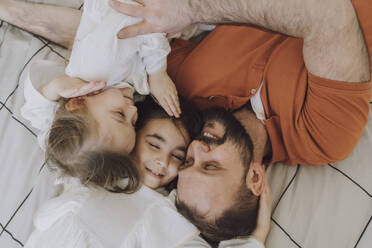 Glücklicher Vater umarmt Töchter auf dem Bett zu Hause - VBUF00288