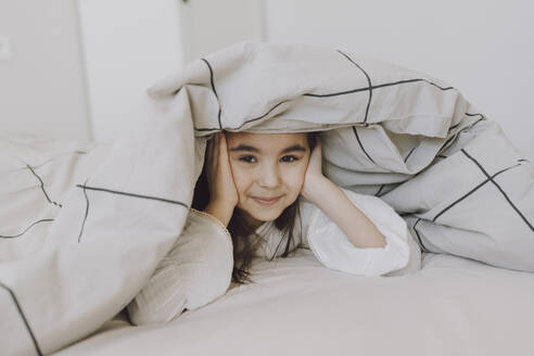 Smiling cute girl lying under blanket on bed - VBUF00290