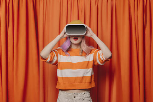 Surprised woman wearing virtual reality simulator standing in front of orange curtain - VSNF00678