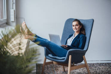 Lächelnde Geschäftsfrau mit Laptop auf einem Sessel sitzend - JOSEF18388