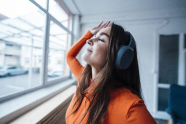 Carefree businesswoman wearing headphones enjoying music in office - JOSEF18415
