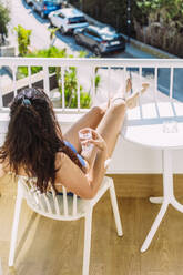 Frau mit einem Glas Wasser auf einem Balkon sitzend - EGHF00740