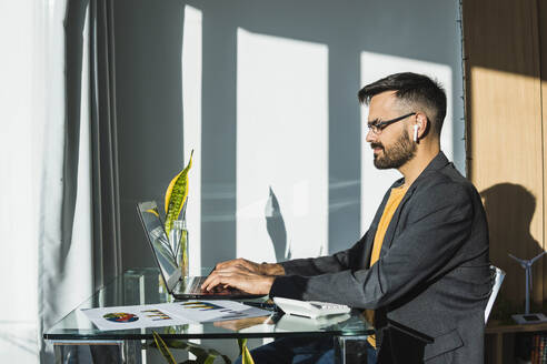 Geschäftsmann arbeitet an einem Laptop am Schreibtisch im Büro zu Hause - MGRF00911