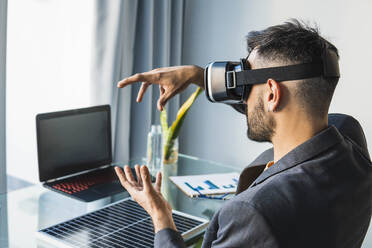 Businessman wearing virtual reality headset at home office - MGRF00919