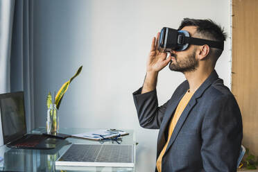 Geschäftsmann, der ein Virtual-Reality-Headset im Büro zu Hause einstellt - MGRF00920