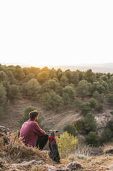 Mann schaut auf Landschaft mit Hund bei Sonnenuntergang - MGRF00929