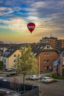 Deutschland, Nordrhein-Westfalen, Grevenbroich, Wohnviertel in der Abenddämmerung mit Heißluftballon im Hintergrund - FRF01012