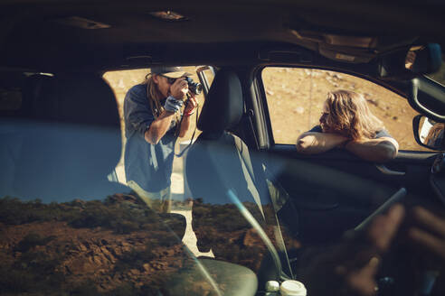 Man photographing friend leaning on car window - KOF00050