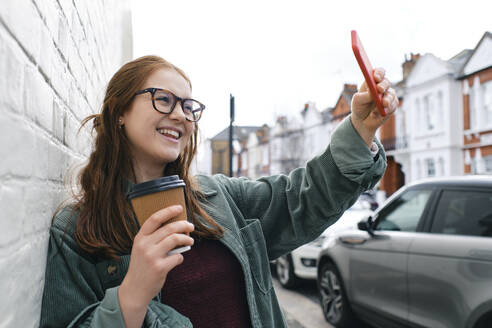 Fröhliche Frau fängt einen Moment mit ihrer Smartphone-Kamera ein und lächelt für ein Selfie - ASGF03546