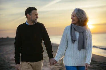 glückliches reifes Paar, das sich an den Händen hält und am Strand spazieren geht - EBSF03137