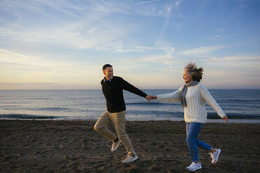 Fröhliches reifes Paar hält sich an den Händen und läuft an der Küste - EBSF03142