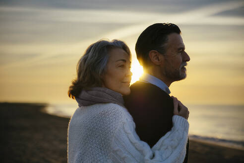 Smiling mature woman and man enjoying sunrise at beach - EBSF03151