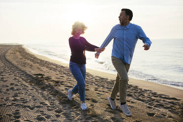 Cheerful mature woman running with man at coastline - EBSF03168