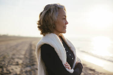 Thoughtful mature woman with arms crossed standing at beach - EBSF03173