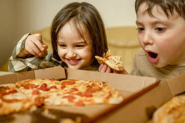 Happy boy eating pizza with brother at home - ANAF01197