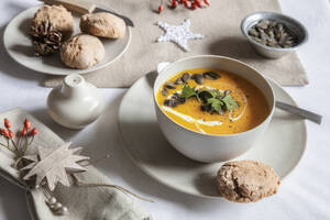 Studioaufnahme einer Schüssel Kürbissuppe mit hausgemachten Brötchen in weihnachtlicher Umgebung - EVGF04316