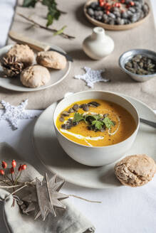 Studioaufnahme einer Schüssel Kürbissuppe mit hausgemachten Brötchen in weihnachtlicher Umgebung - EVGF04317