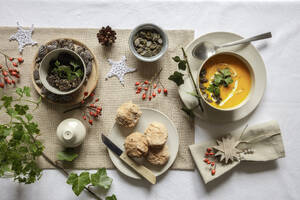 Studioaufnahme einer Schüssel Kürbissuppe mit hausgemachten Brötchen in weihnachtlicher Umgebung - EVGF04323