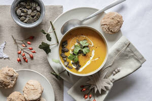 Studioaufnahme einer Schüssel Kürbissuppe mit hausgemachten Brötchen in weihnachtlicher Umgebung - EVGF04326