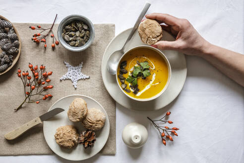 Hand einer Frau, die eine Schüssel Kürbissuppe mit hausgemachten Brötchen isst - EVGF04327