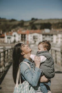 Happy mother carrying son at jetty on sunny day - MTBF01268