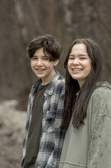 Lächelnde Teenager-Geschwister in Freizeitkleidung an einem regnerischen Tag - ANAF01205