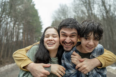 Glücklicher Vater umarmt Sohn und Tochter im Teenageralter - ANAF01214
