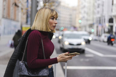 Frau mit Smartphone auf dem Bürgersteig wartend - JJF00751