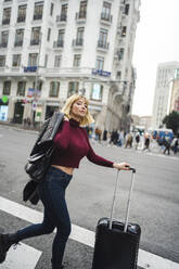 Frau mit Gepäckwagen beim Überqueren der Straße in der Stadt - JJF00757