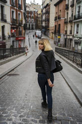 Frau schaut über die Schulter beim Gehen auf der Straße in der Stadt - JJF00770