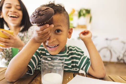 Verspielter Junge genießt Cupcake mit Mutter zu Hause - JCCMF10255