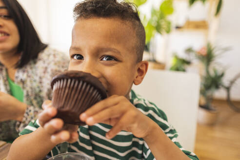 Junge isst Schokoladen-Cupcake zu Hause - JCCMF10256