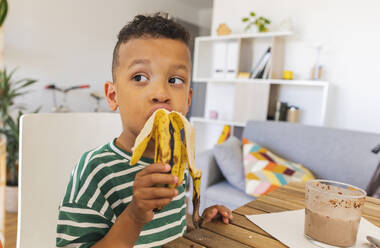 Nachdenklicher Junge isst Banane zu Hause - JCCMF10266