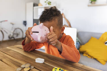 Boy opening piggy bank to count coins at home - JCCMF10271