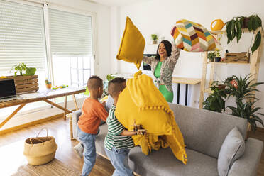 Playful mother playing pillow fight with twin sons at home - JCCMF10285