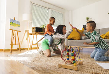 Young woman playing with twin sons in living room at home - JCCMF10295