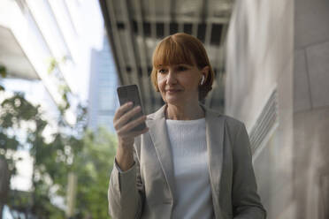 Mature businesswoman using mobile phone outside building - IKF00087