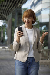 Businesswoman talking on video call through smart phone on footpath - IKF00088